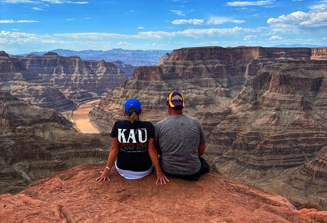 A guy and a girl look down from above at the Grand Canyon and the river