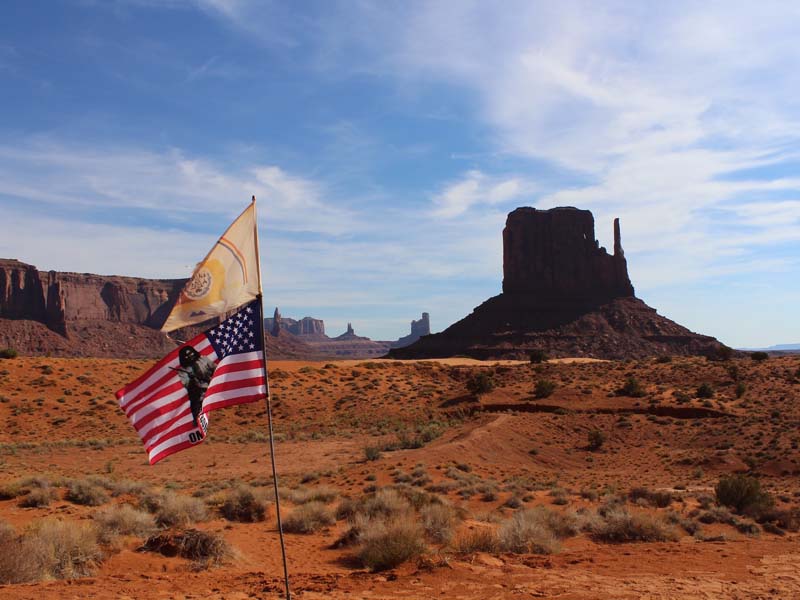 The Navajo Nation flag and American flag flown in front of one of the Mittens Buttes at Monument Valley
